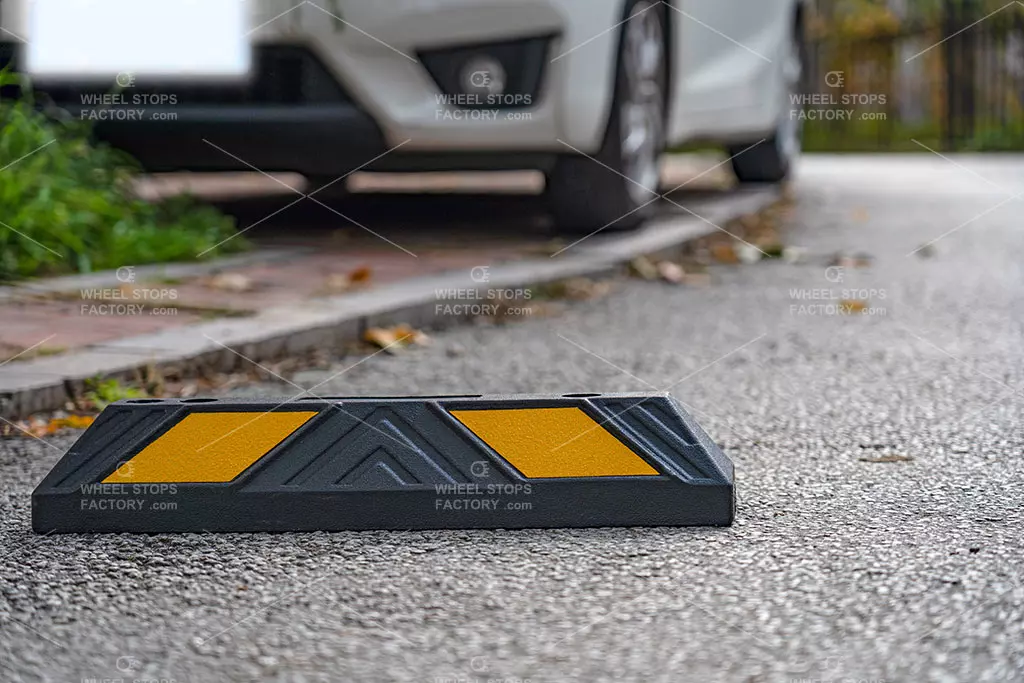 A car park bump stop with two yellow reflective tapes placed near a curb