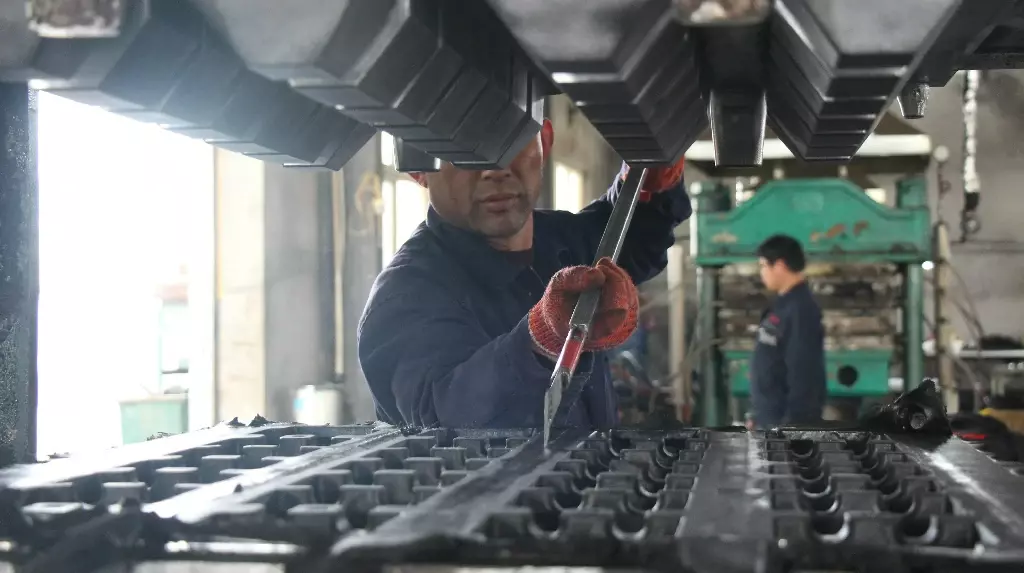 A worker in the Wheel Stops Factory cutting rubber with a steel tool