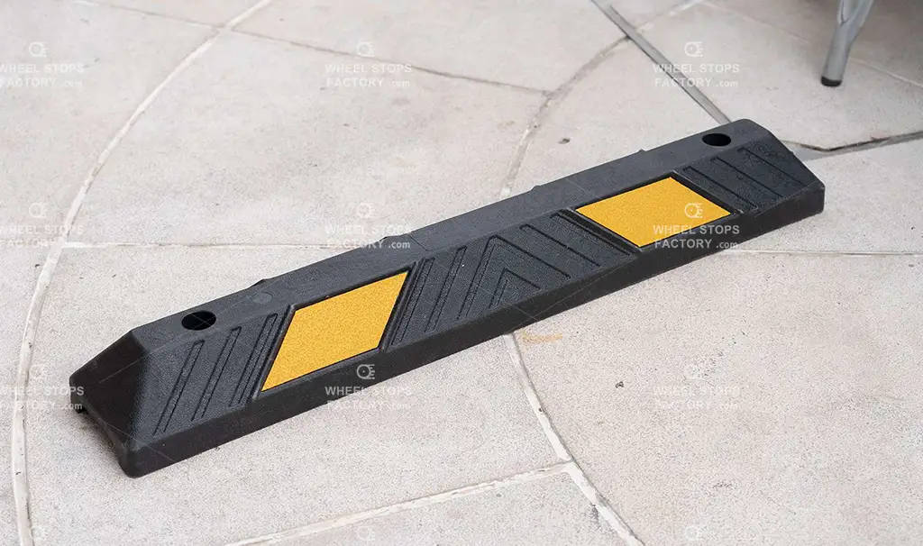 A black parking lot curb stop with yellow reflective films made by Wheel Stops Factory.